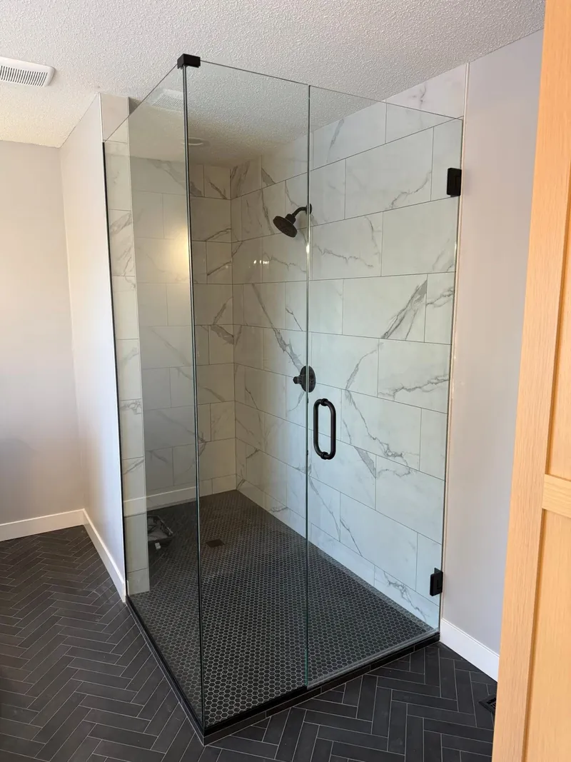 Frameless glass shower door with black hinges and handle, installed by MN Glass