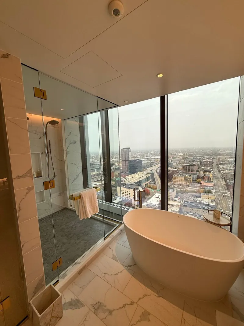 Glass shower wall next to a tub and a window with a city view
